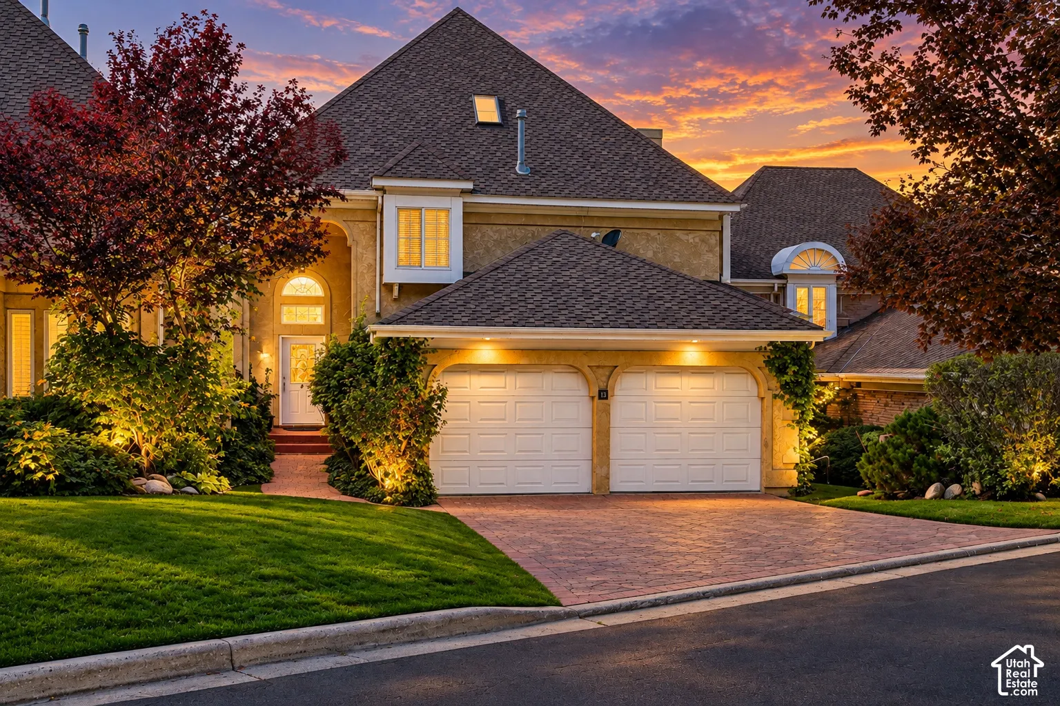 Elegant two-story residence featuring a steeply pitched gable roof with architectural dormers, illuminated by landscape lighting that accentuates the home's exterior