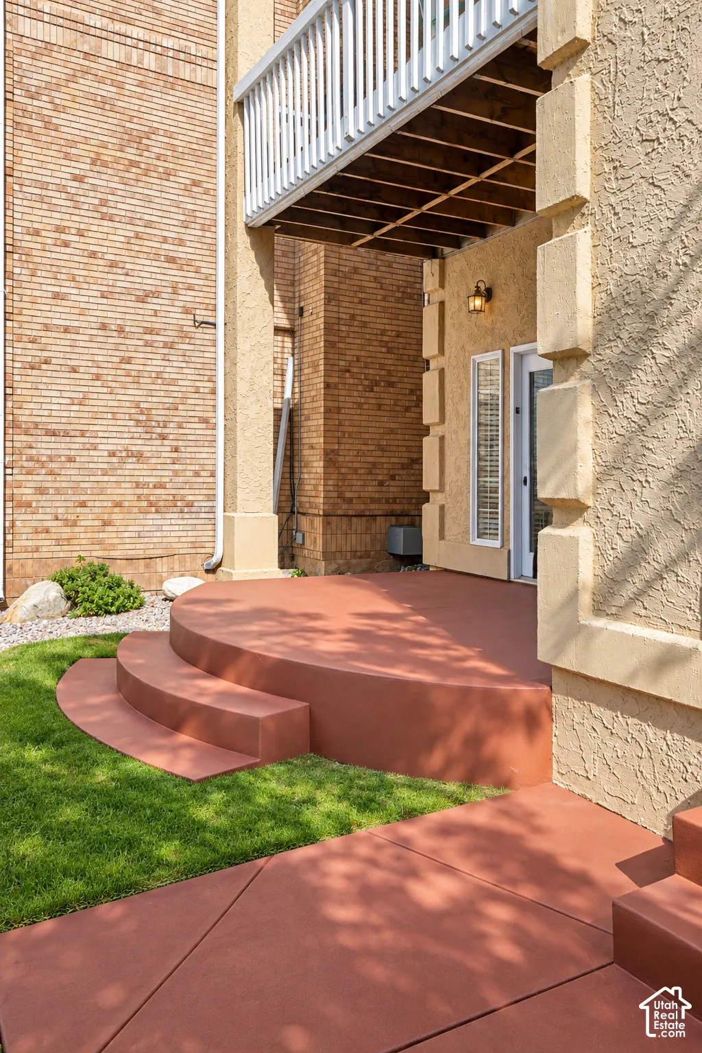 Ground-level patio with steps, complemented by a manicured lawn and a stucco exterior with an outdoor light fixture