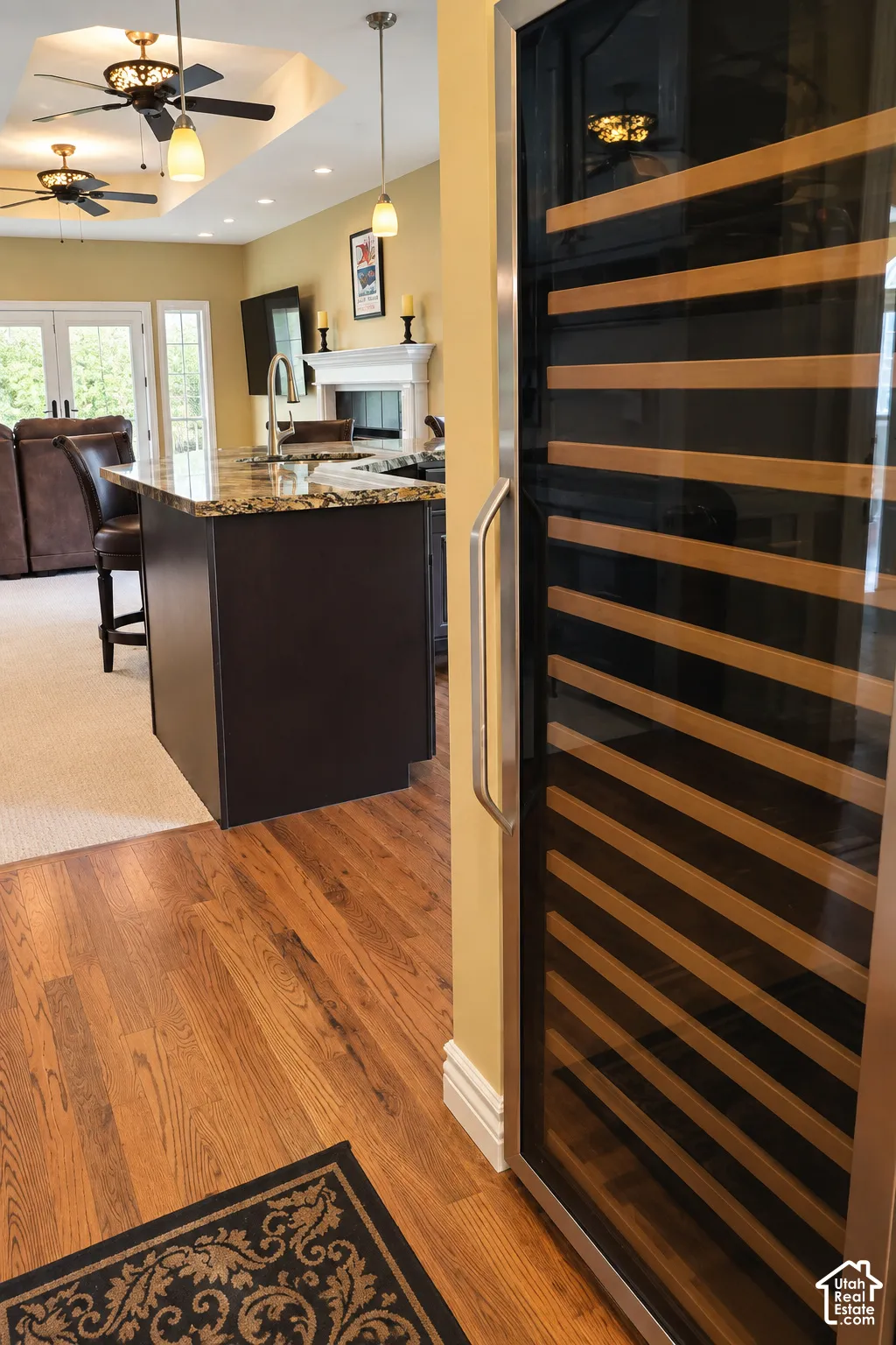 Built-in beverage cooler with glass door, hardwood flooring, kitchen island with stone countertop, recessed lighting, and tray ceiling