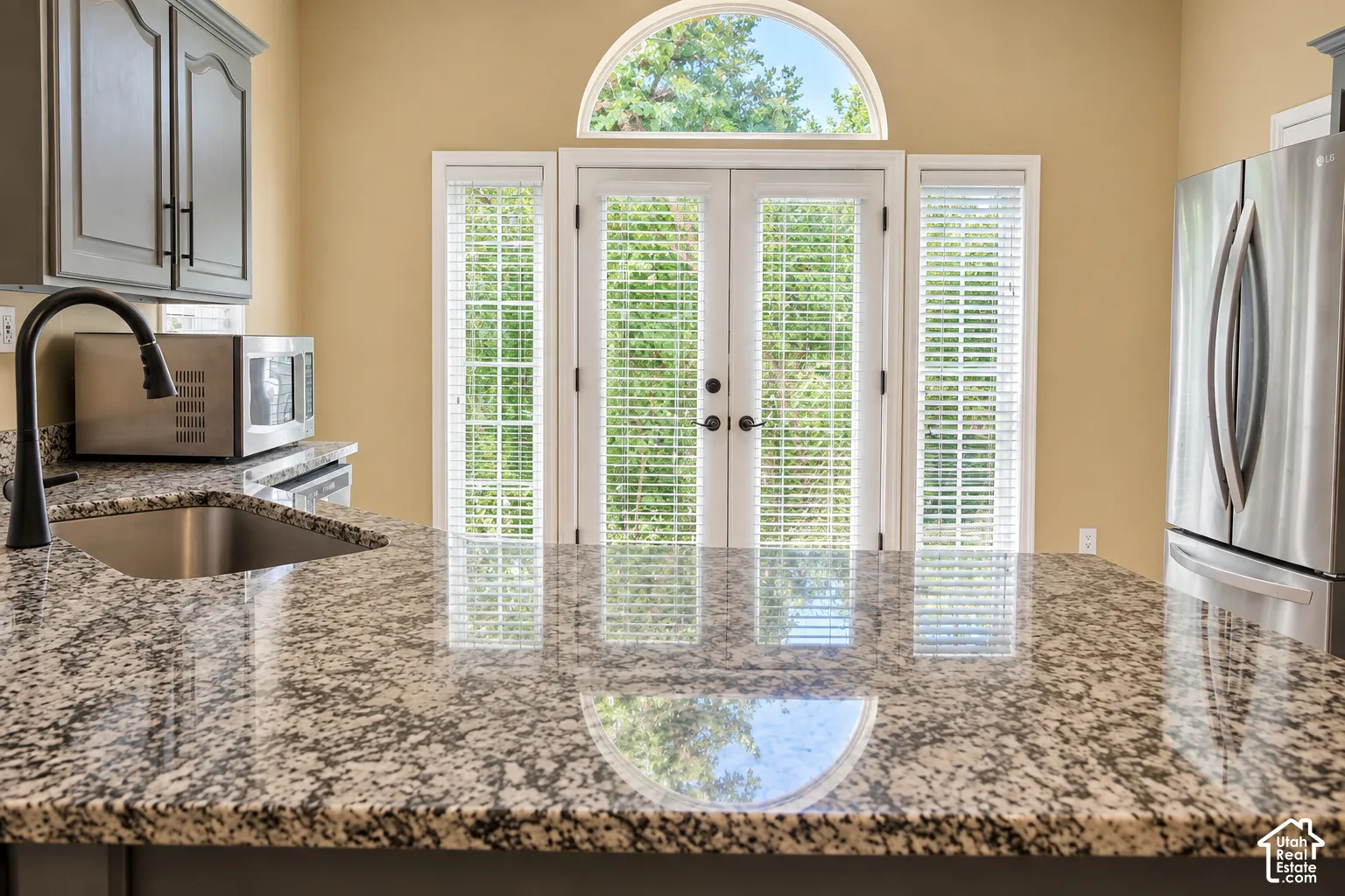 Sophisticated kitchen showcasing a speckled stone countertop with waterfall edge, stainless steel appliances, and a bronze pull-down faucet