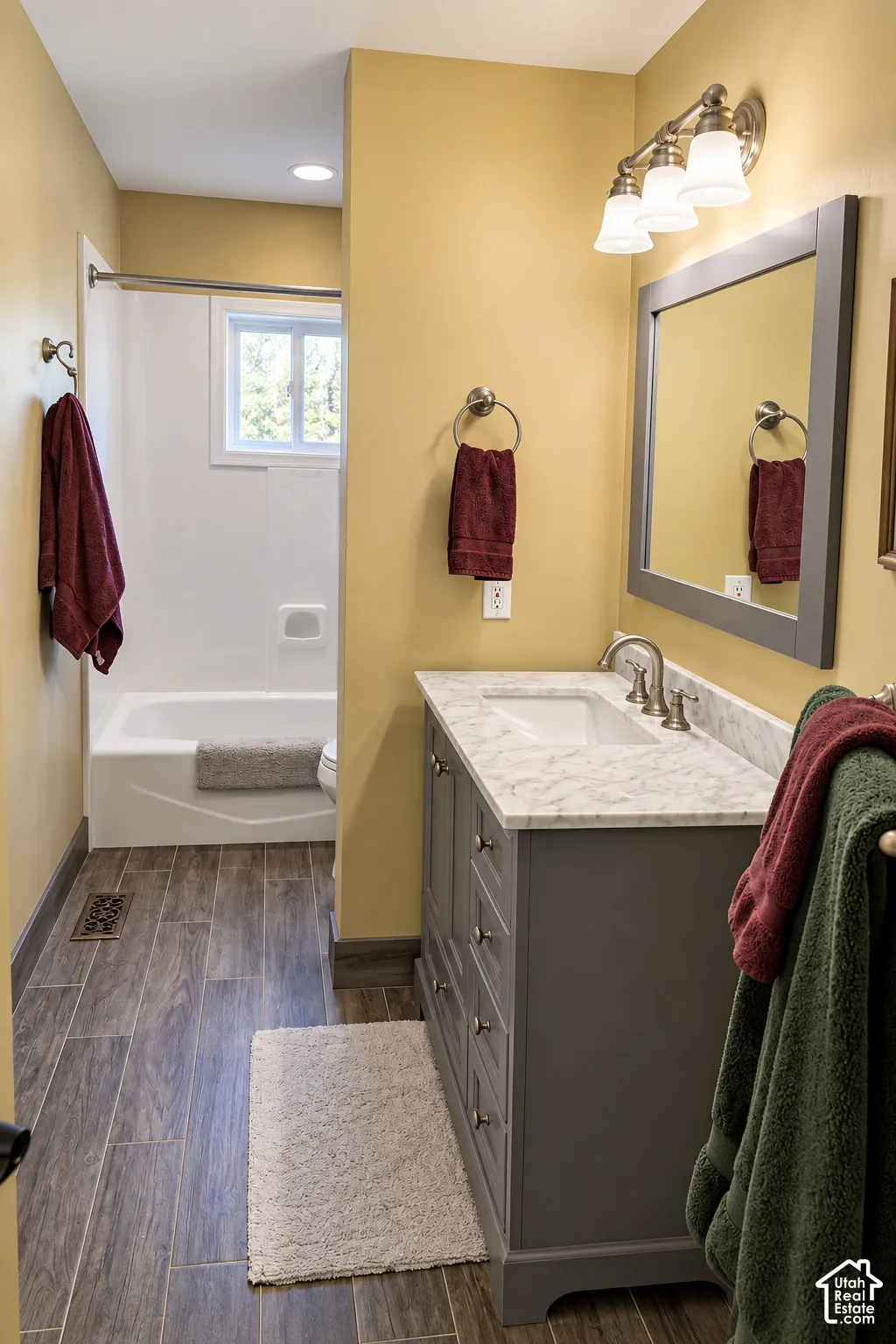 Bathroom featuring a single vanity with a white countertop, wood-finish flooring, a white bathtub, and a window