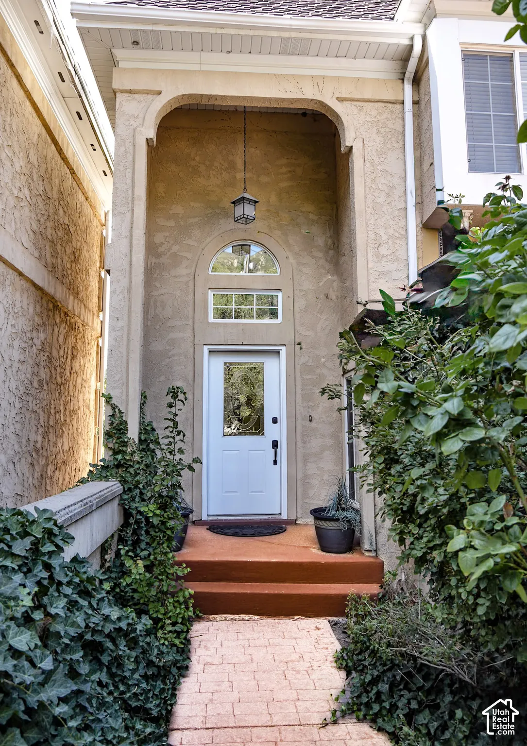 Covered entryway with arched stucco detailing, an arched transom window, and a white paneled door