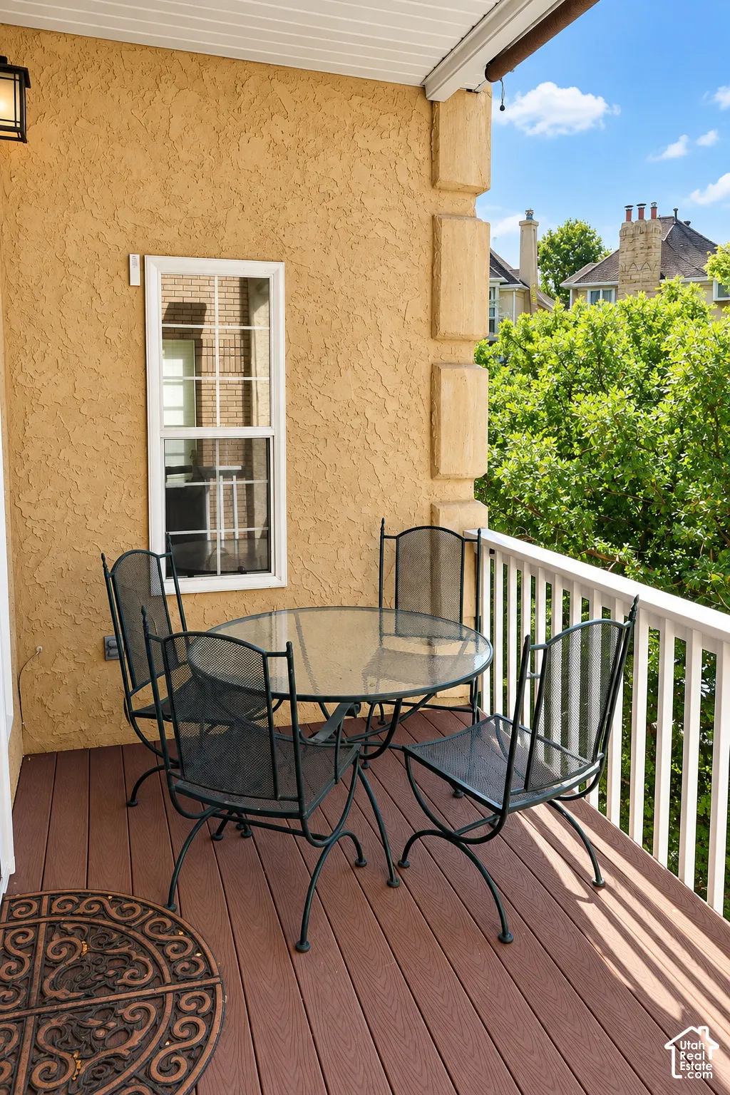 Exterior balcony with wood-finish decking, white railings, and stucco wall finish