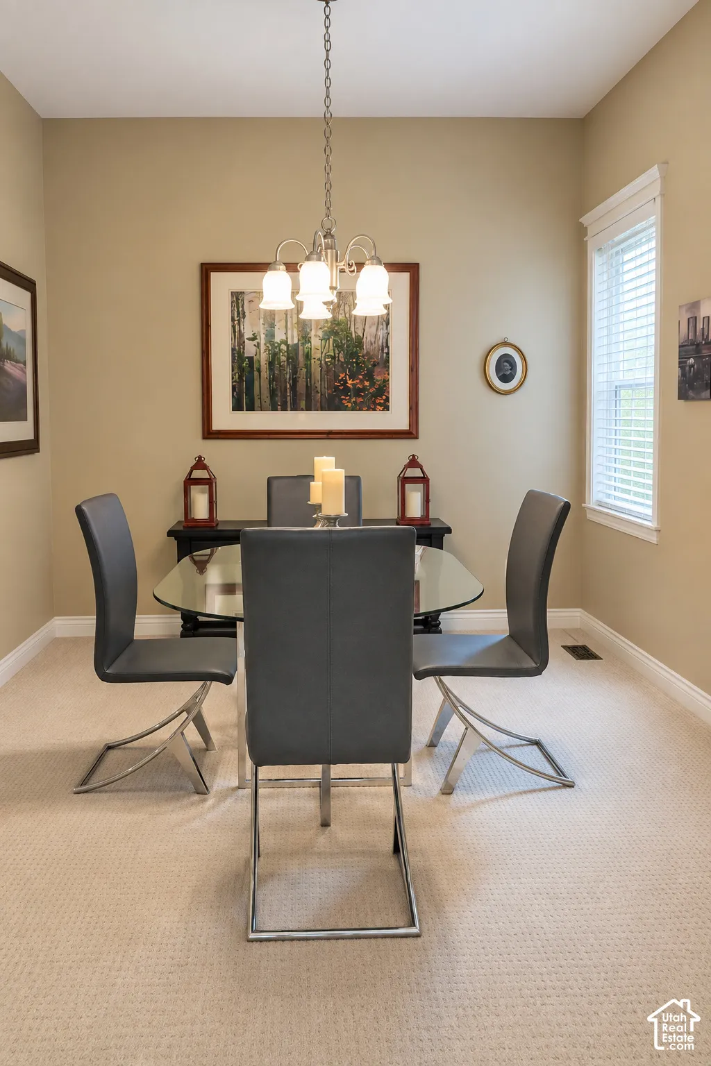 Formal dining space featuring a round black pedestal table, contemporary chrome-leg dining chairs, neutral carpet flooring, warm beige walls, pendant lighting fixture, and large windows providing natural light
