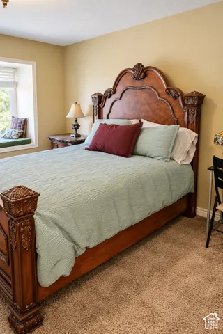 Elegant bedroom showcasing a carved wood bed frame with upholstered headboard, soft-close cabinetry, warm yellow walls, carpeted flooring, and abundant natural light from a large window