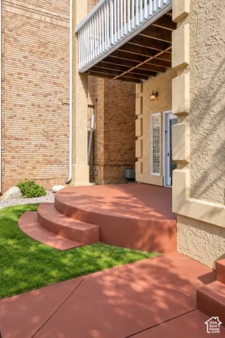 Ground-level patio with steps, complemented by a manicured lawn and a stucco exterior with an outdoor light fixture