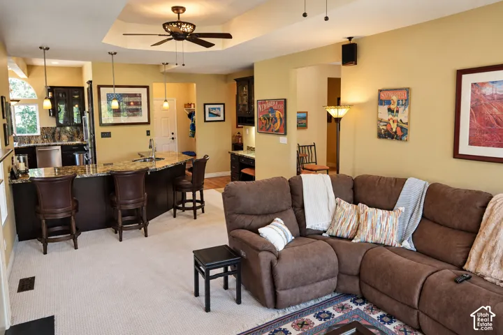 Kitchen island with integrated bar seating, recessed ceiling with a ceiling fan, pendant lighting, and light-colored carpeting