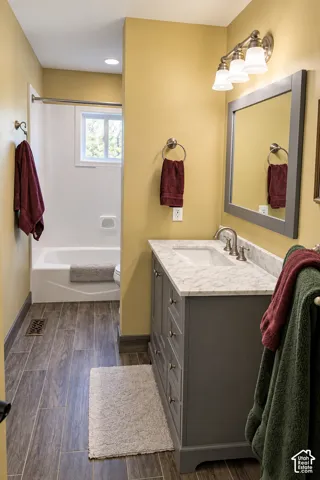 Bathroom featuring a single vanity with a white countertop, wood-finish flooring, a white bathtub, and a window