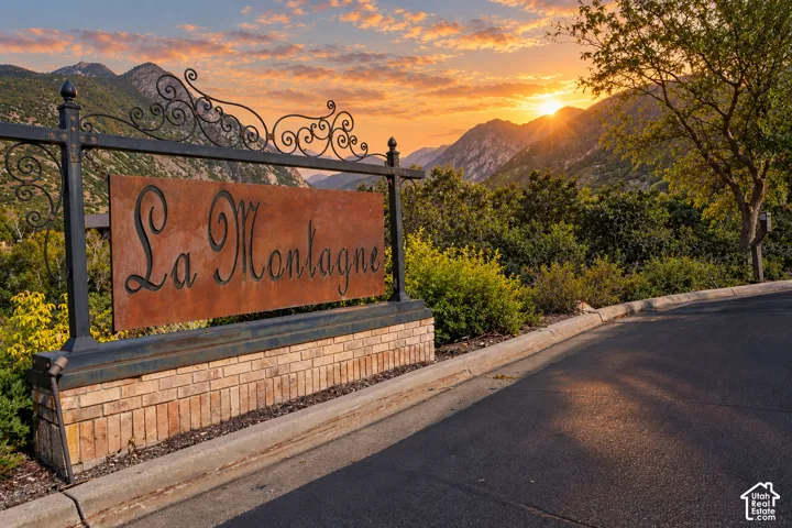 Gated entrance featuring ornamental wrought-iron detailing and brick-base construction, framed by mature landscaping and mountain backdrop at sunset