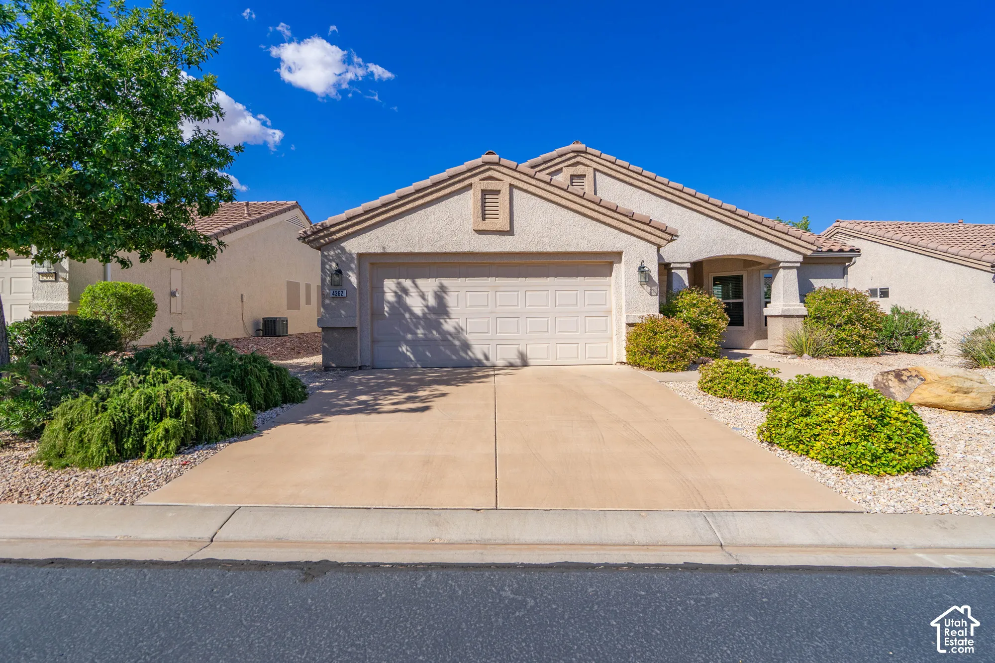 Stucco exterior with a tile roof, an integrated two-car garage, a covered entry, and xeriscaped landscaping