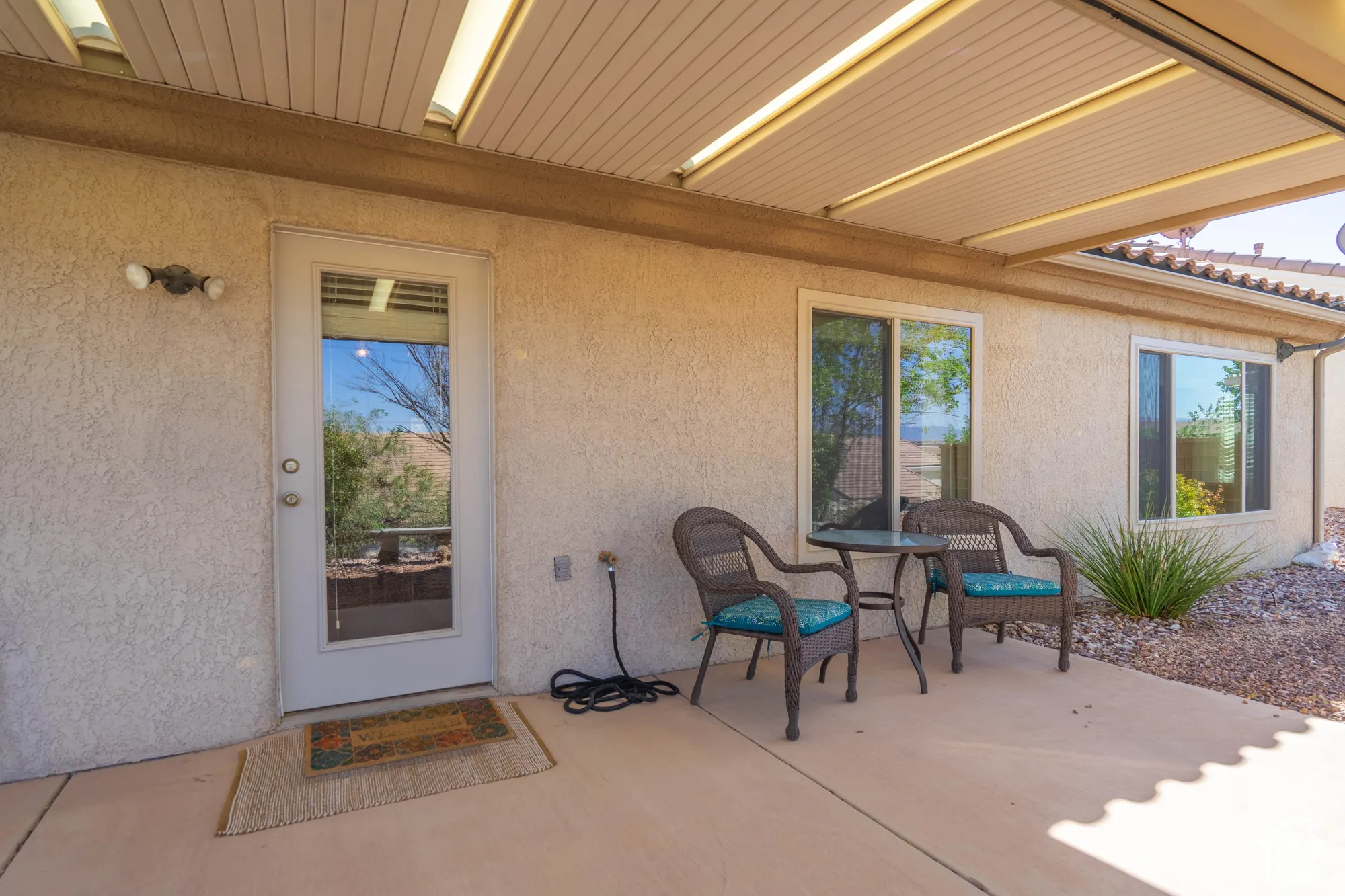 Covered patio with textured stucco exterior, full-lite glass door, sliding windows, and tiled roofline