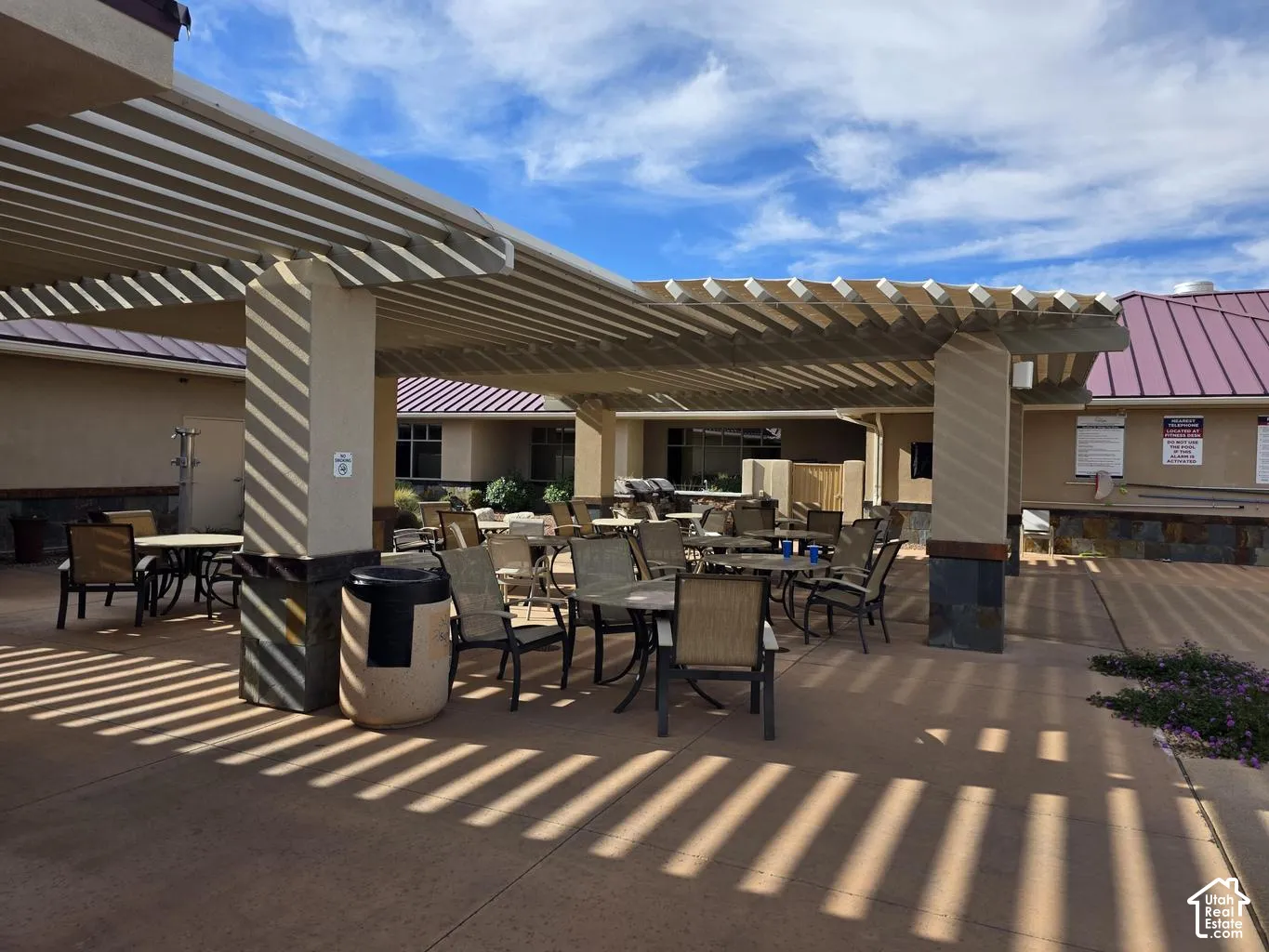 Expansive outdoor patio with a slatted pergola cover, stucco columns with stone bases, and a textured concrete surface