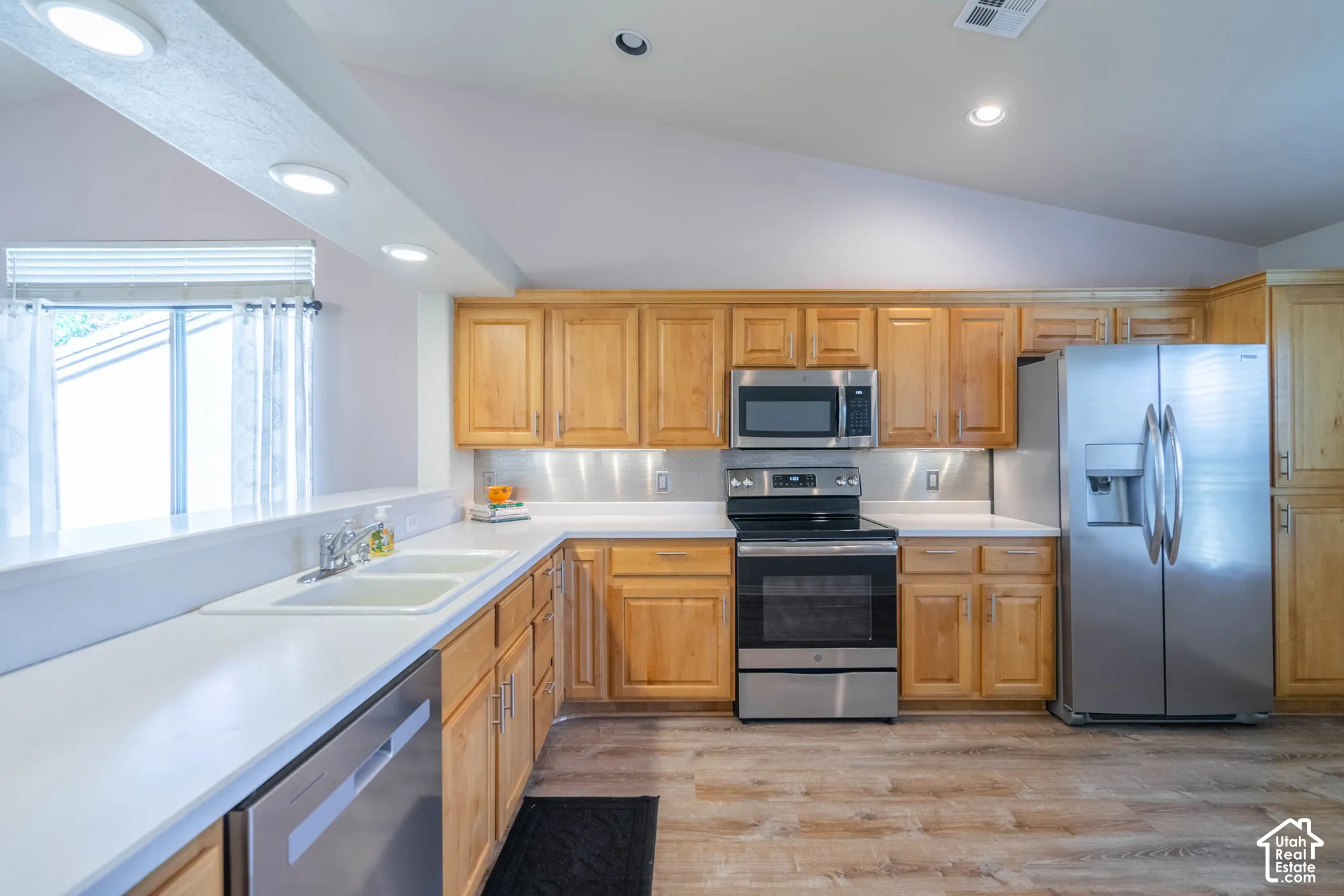 Kitchen featuring alder cabinetry, stainless steel appliances, white Corian countertops, and wood-finish LVP flooring