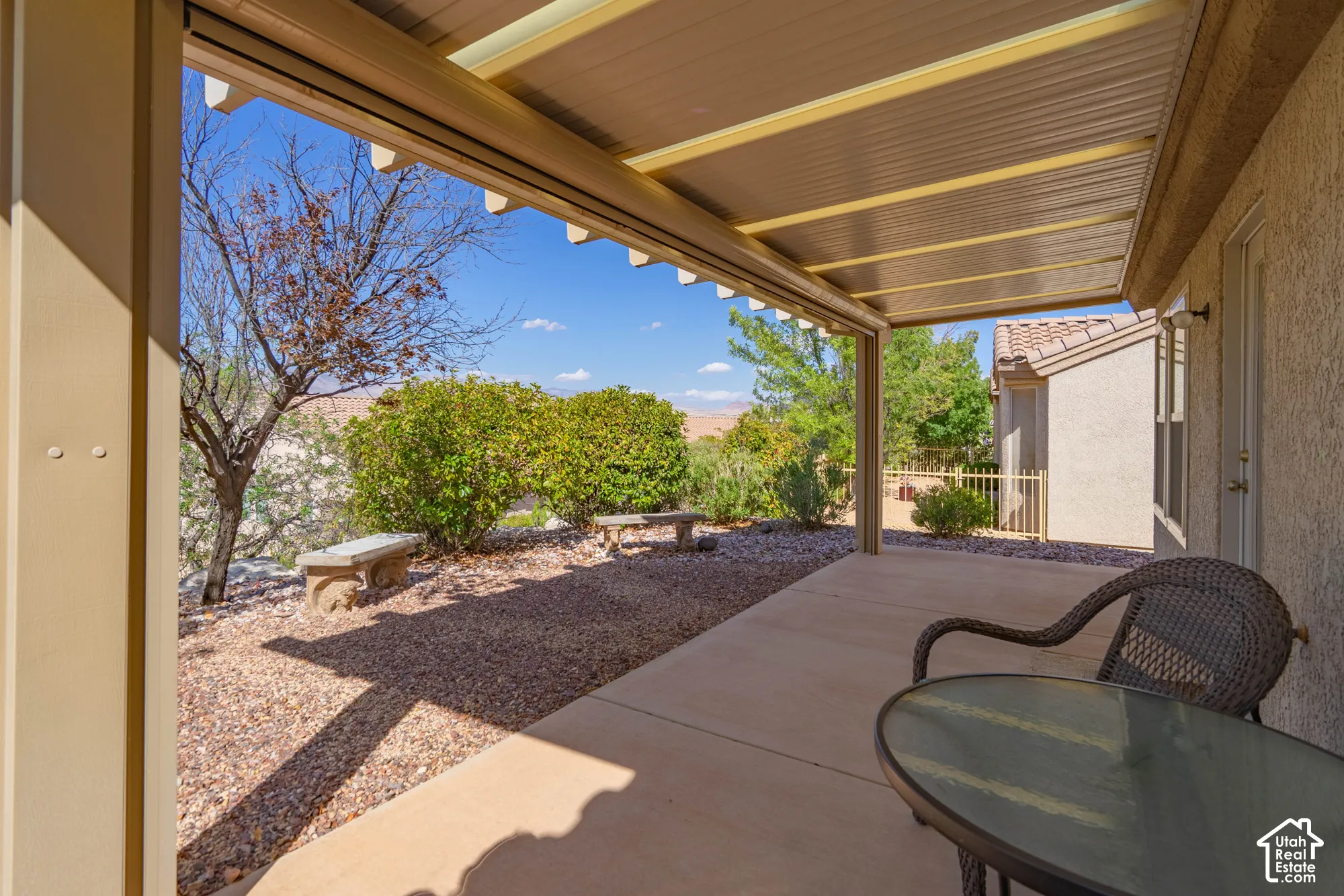 Covered patio with concrete flooring, gravel landscaping, and mature shrubbery