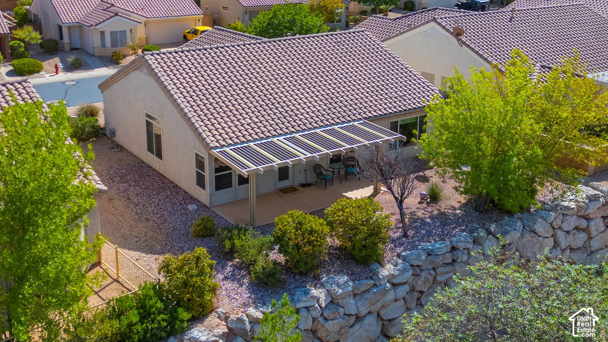 Rear exterior with a covered patio, tiled roofing, solar panels, and a rock retaining wall