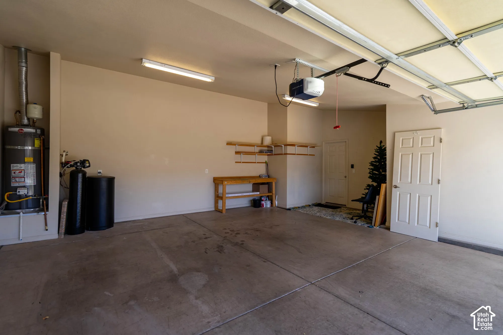 Spacious garage with concrete flooring, built-in shelving, water heater, and garage door opener