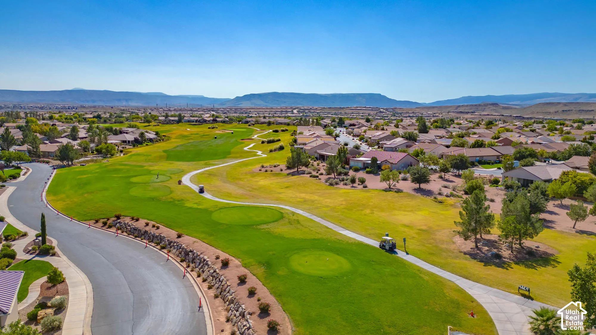 Expansive golf course frontage with manicured greens and fairways, surrounded by residential properties and desert landscaping, all set against a distant mountain range