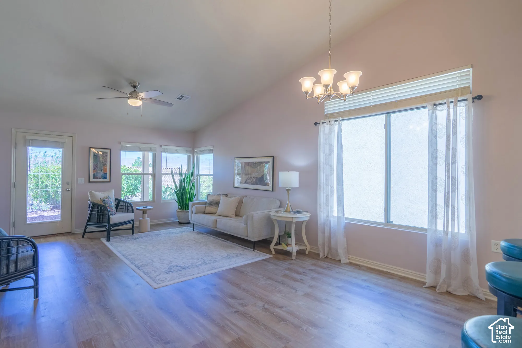 Living and Dining Room with vaulted ceiling with an attached ceiling fan, wood-finish flooring, multiple large windows, and a glass-paneled door