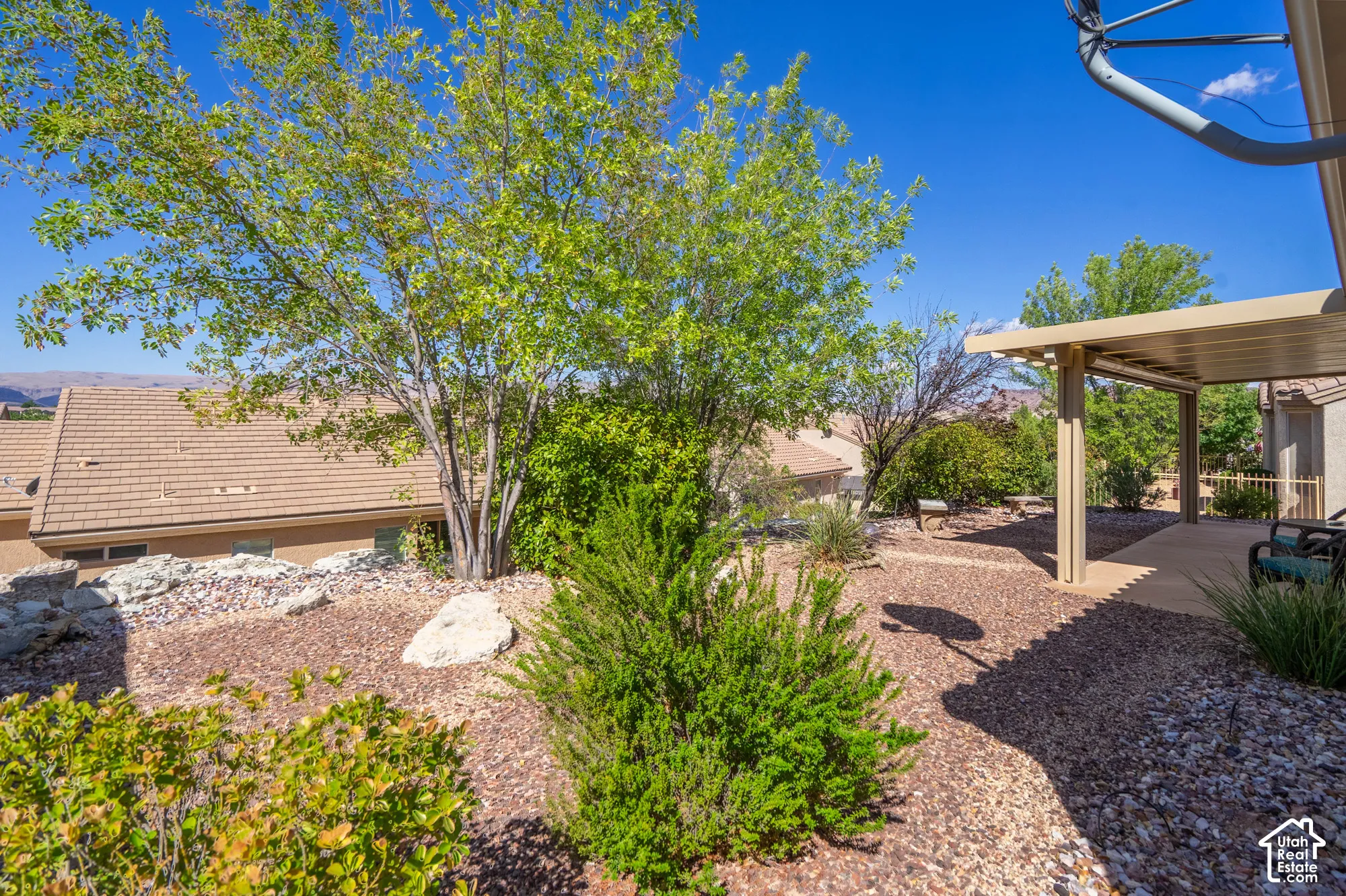 Outdoor living area featuring a covered patio, xeriscaped landscaping with mature trees, and a gravel pathway