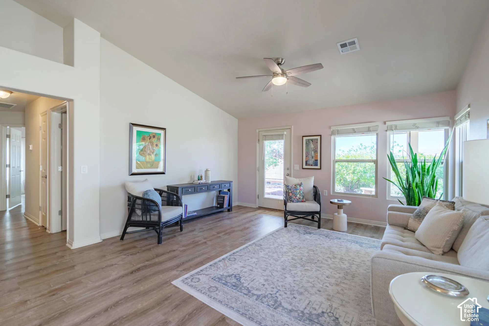 Vaulted ceilings, wood-finish flooring, ceiling fan with integrated lighting, multiple windows, and a glass-paneled exterior door