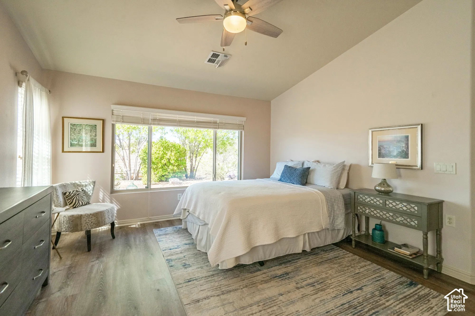 Primary Bedroom with Vaulted ceiling, ceiling fan, large window, wood-finish LVP flooring, and white window blinds