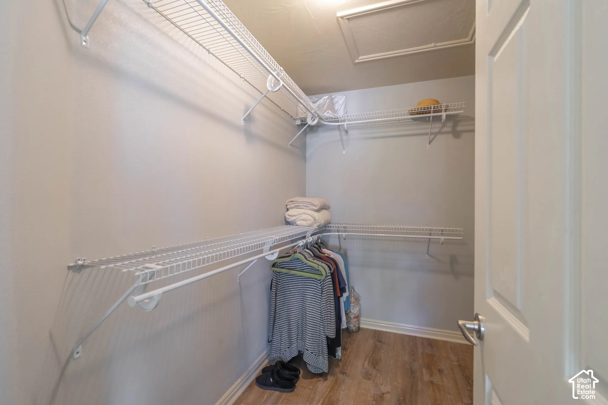 Walk-in closet with multiple wire shelving units and hanging rods, wood-finish flooring, and a paneled door with brushed nickel hardware