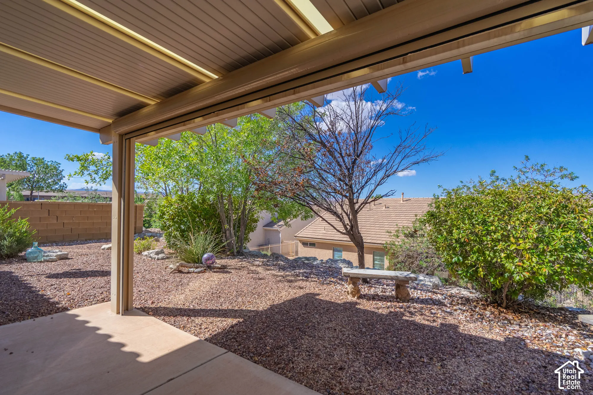 Covered patio with a concrete slab, gravel landscaping, and established trees