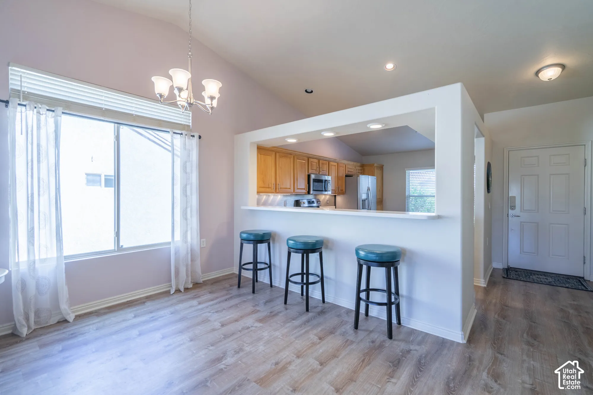 Vaulted ceilings, wood-finish flooring, kitchen pass-through with breakfast bar, wood cabinetry, and stainless steel appliances