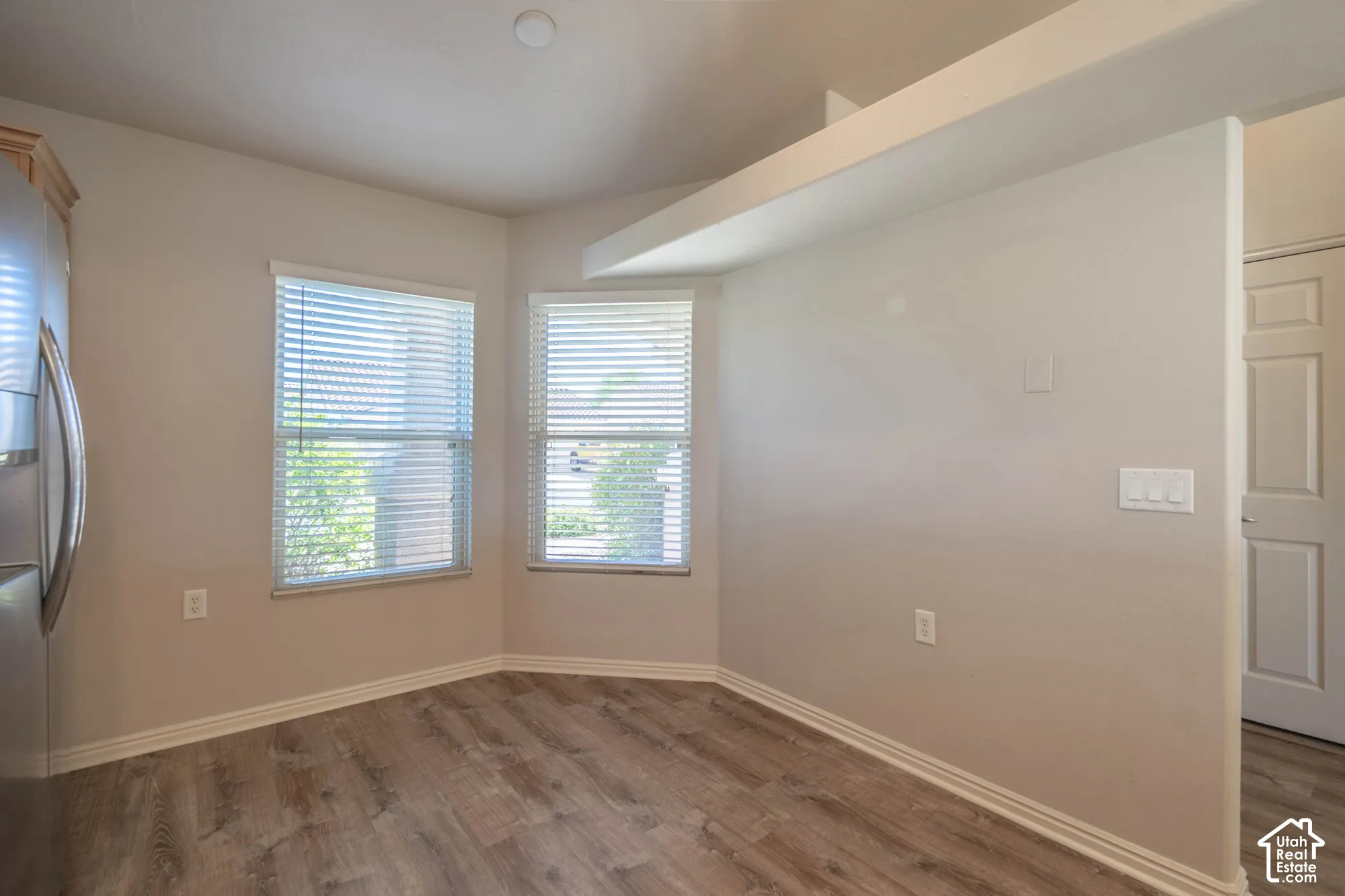 Wood-finish flooring, two large windows with blinds, recessed ceiling lighting, in the kitchen nook