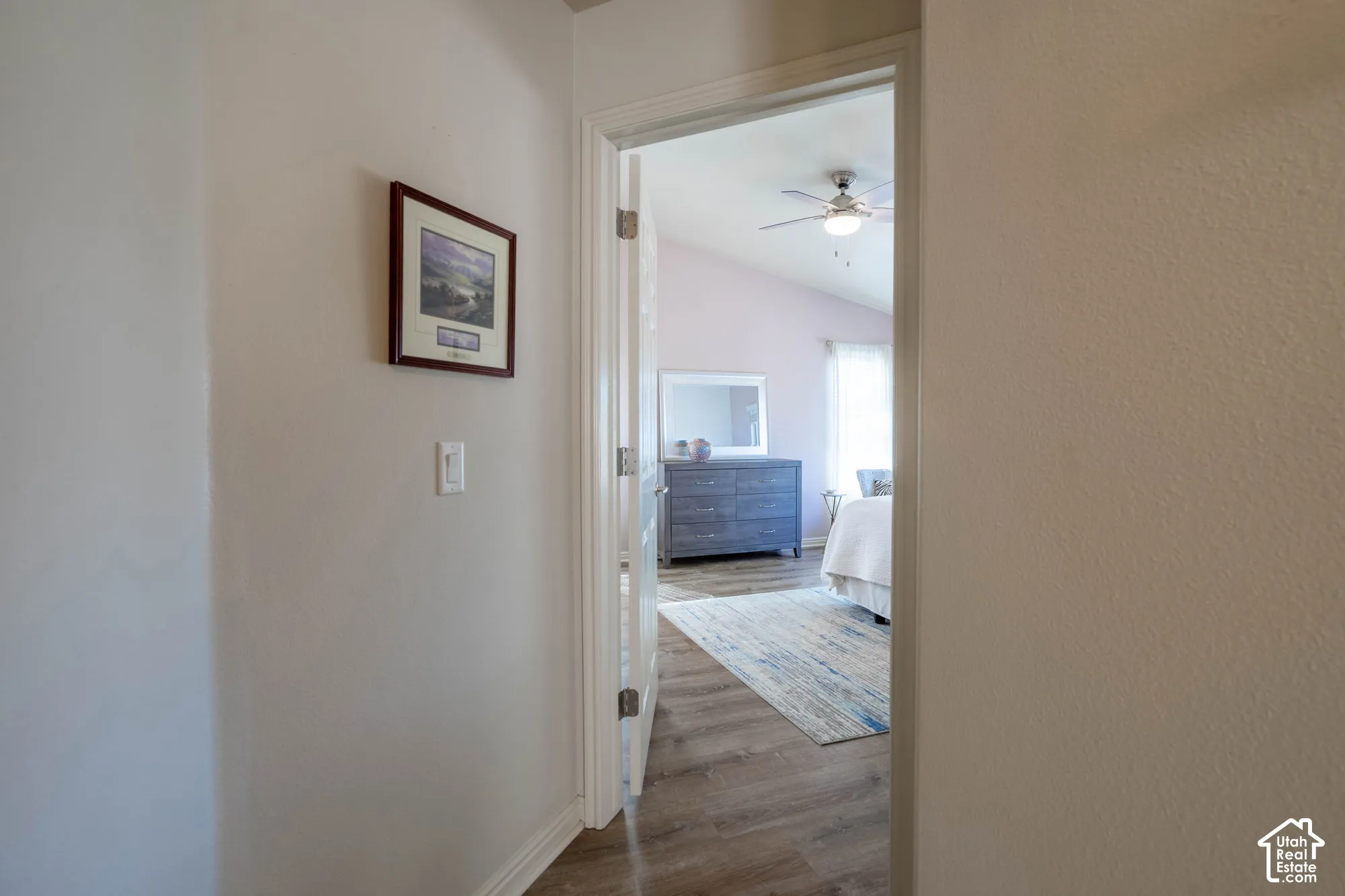 Wood-finish flooring extending into the Primary Bedroom, vaulted ceiling with a ceiling fan, and light-toned walls