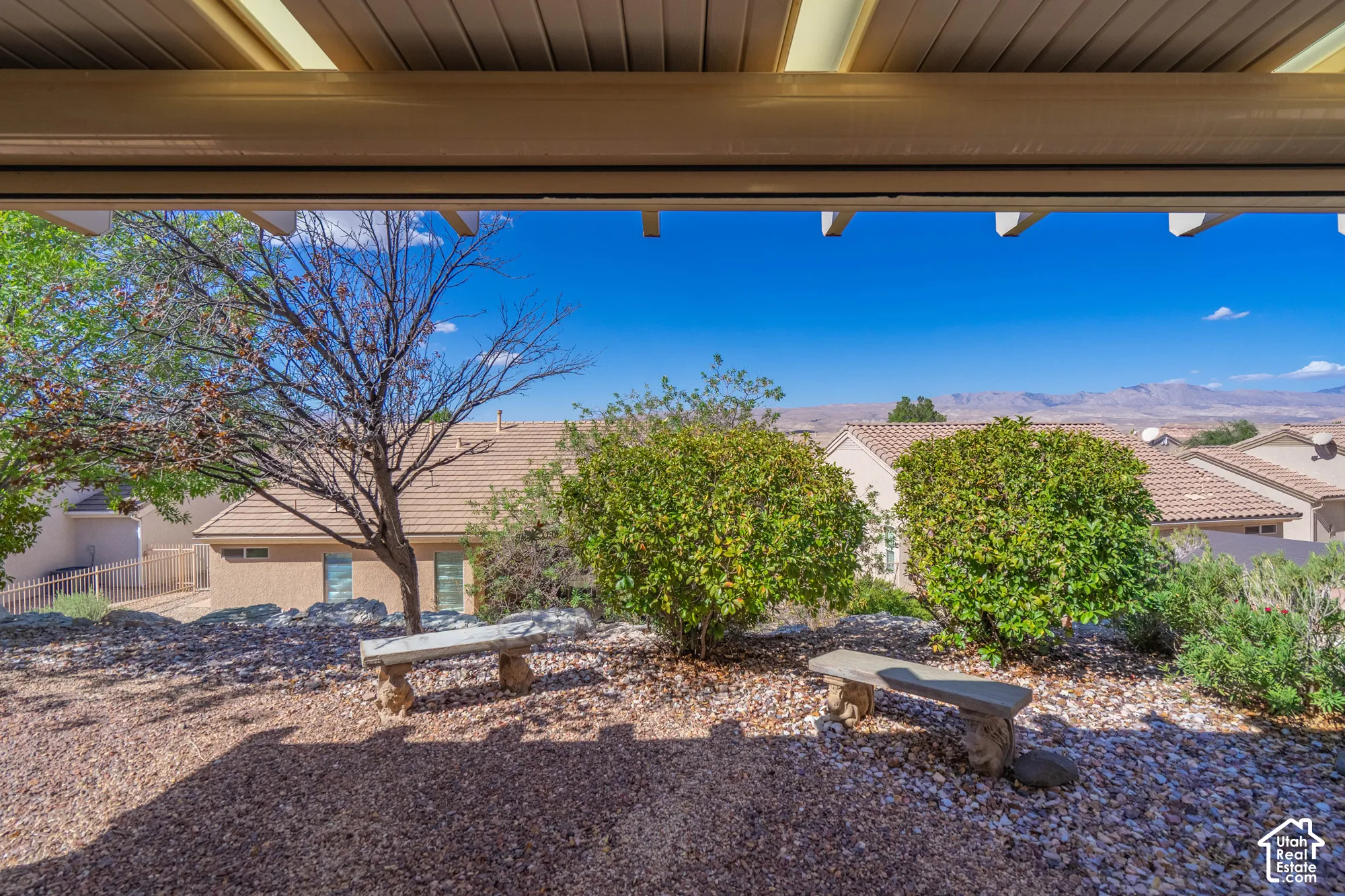Patio with slatted overhead structure, gravel ground cover, and surrounding landscaping, including mountain