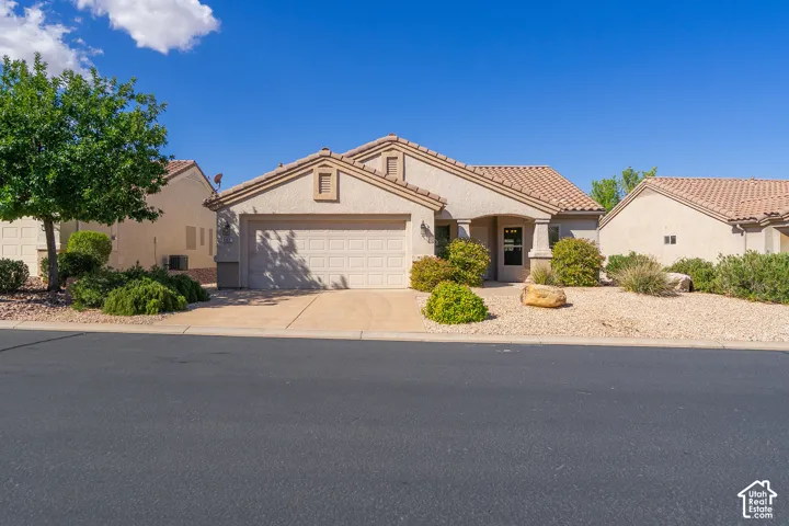 Stucco exterior with a tile roof, an integrated garage, a covered entry, and xeriscape landscaping