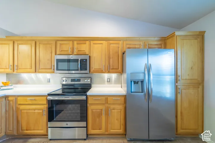 Honey-toned alder cabinetry, stainless steel appliances, white Corian countertops, under cabinet lighting, and wood-finish flooring
