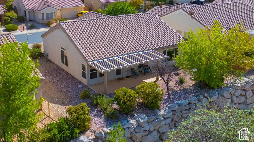 Rear exterior with a covered patio, tiled roofing, solar panels, and a rock retaining wall
