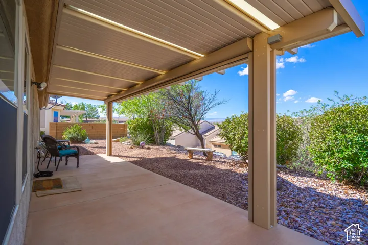 Covered patio with concrete flooring, supported by columns, offering a gravel-landscaped area with mature shrubs