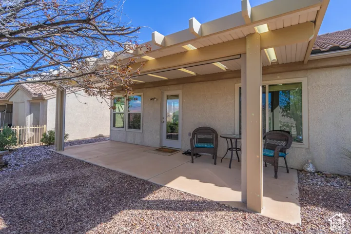 Expansive concrete patio featuring a partial trellis cover, a glass-paneled door, and a large window
