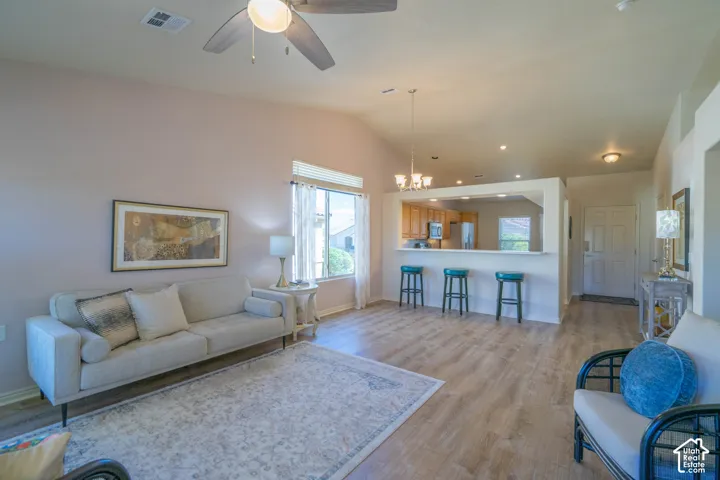 Vaulted ceiling with a ceiling fan, wood-finish flooring, kitchen pass-through with breakfast bar, recessed lighting, and a front entry door