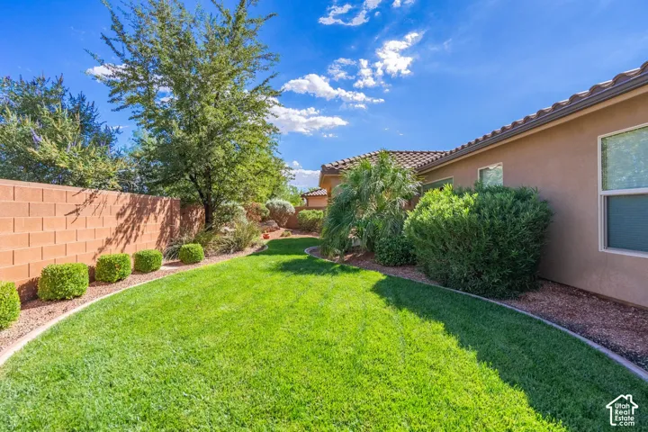 Expansive lawn area with a block privacy fence, mature trees, and well-maintained shrubbery bordering the property