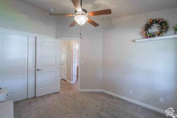 Carpeted room featuring a ceiling fan with light, white interior doors, and a built-in wall shelf