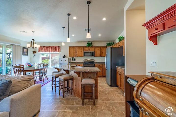 Open-concept kitchen and dining area featuring wood cabinetry, stainless steel appliances, a center island with seating, and terra cotta tile flooring