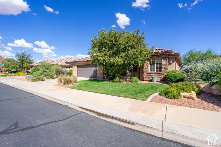 Southwestern-style residence featuring a stucco exterior with clay tile roof accents, positioned on a corner lot with mature landscaping including desert shrubs and ornamental trees
