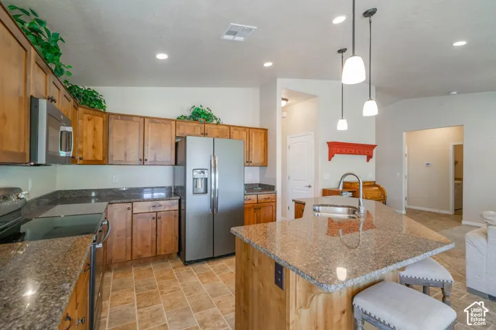 Spacious kitchen featuring warm wood cabinetry, granite countertops, stainless steel appliances including a side-by-side refrigerator, and a large center island with seating