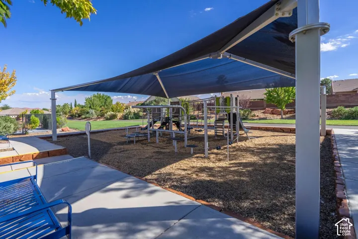 Playground structure with shade canopy, bordered by a concrete pathway and wood chip surfacing