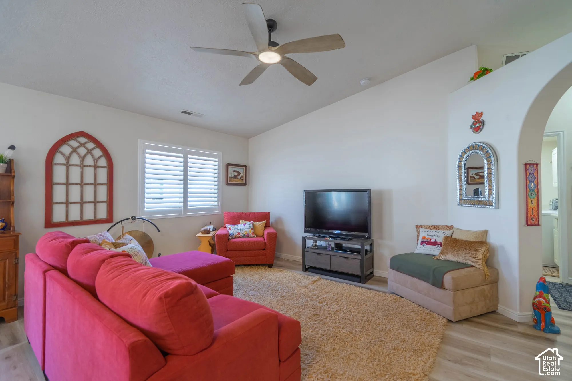 Vaulted ceiling with an integrated ceiling fan, plantation shutters, wood-finish flooring, and an arched doorway