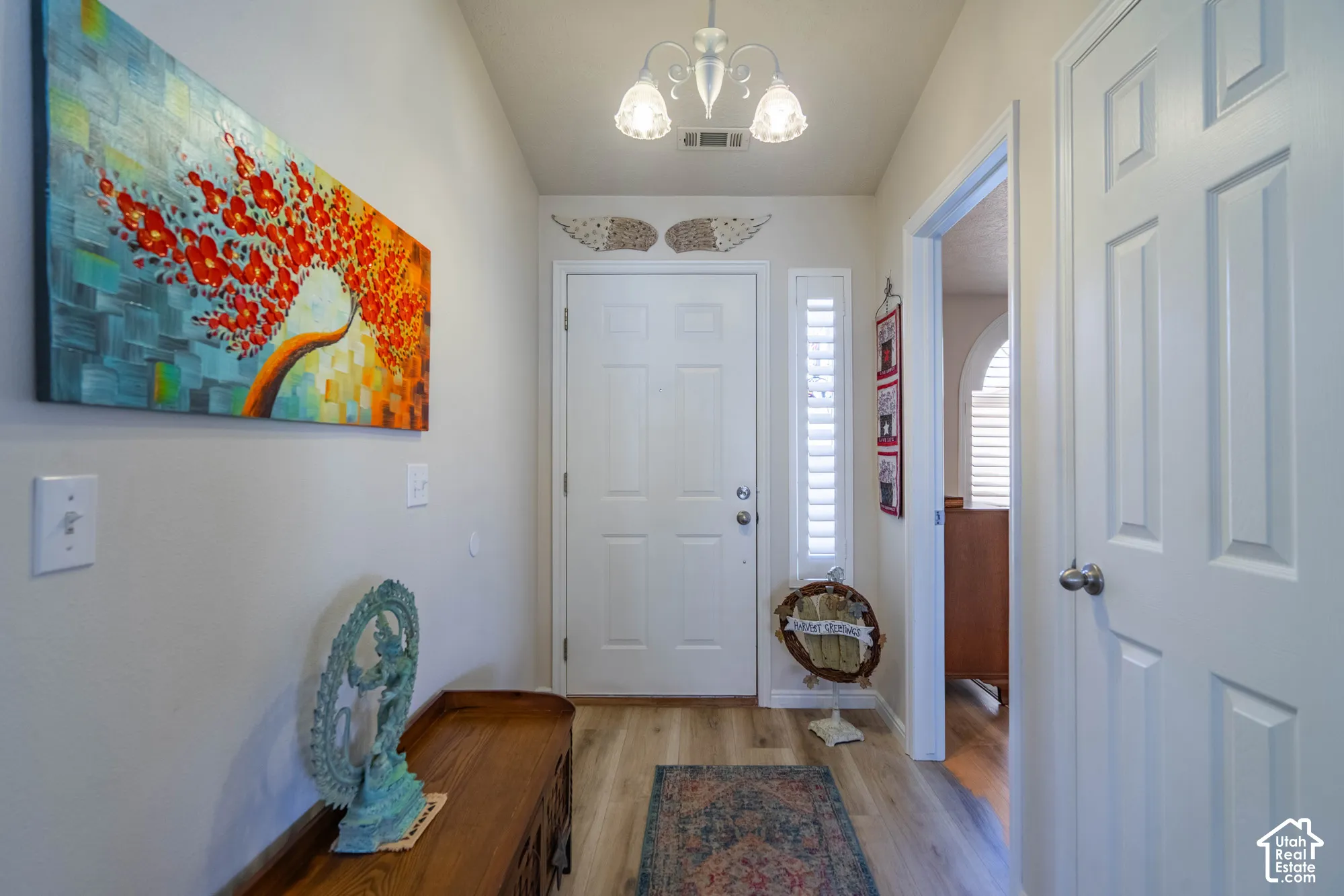 Entryway featuring wood-finish flooring, a decorative overhead light fixture, a sidelight with louvered shutters, and paneled interior doors