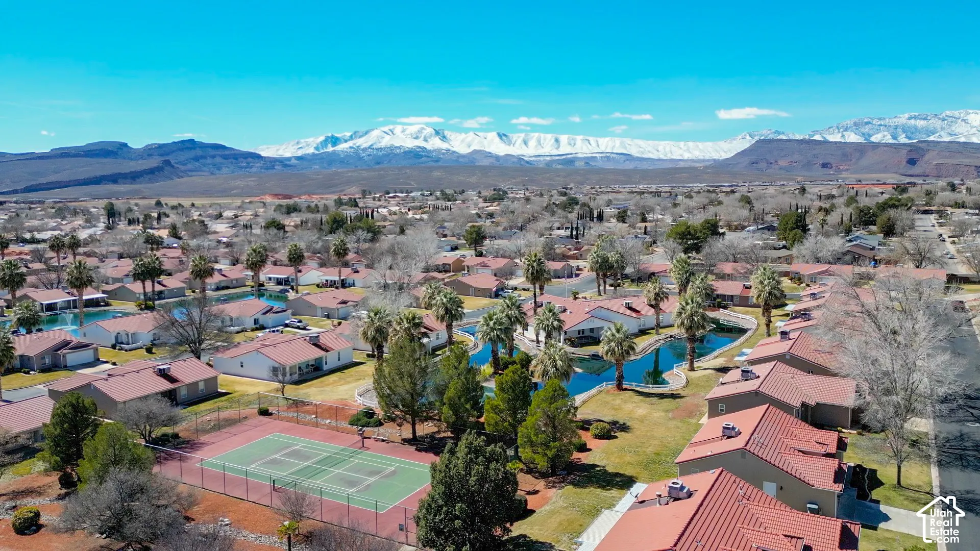 Community with red tile roofs, multiple ponds, tennis court, and desert landscape