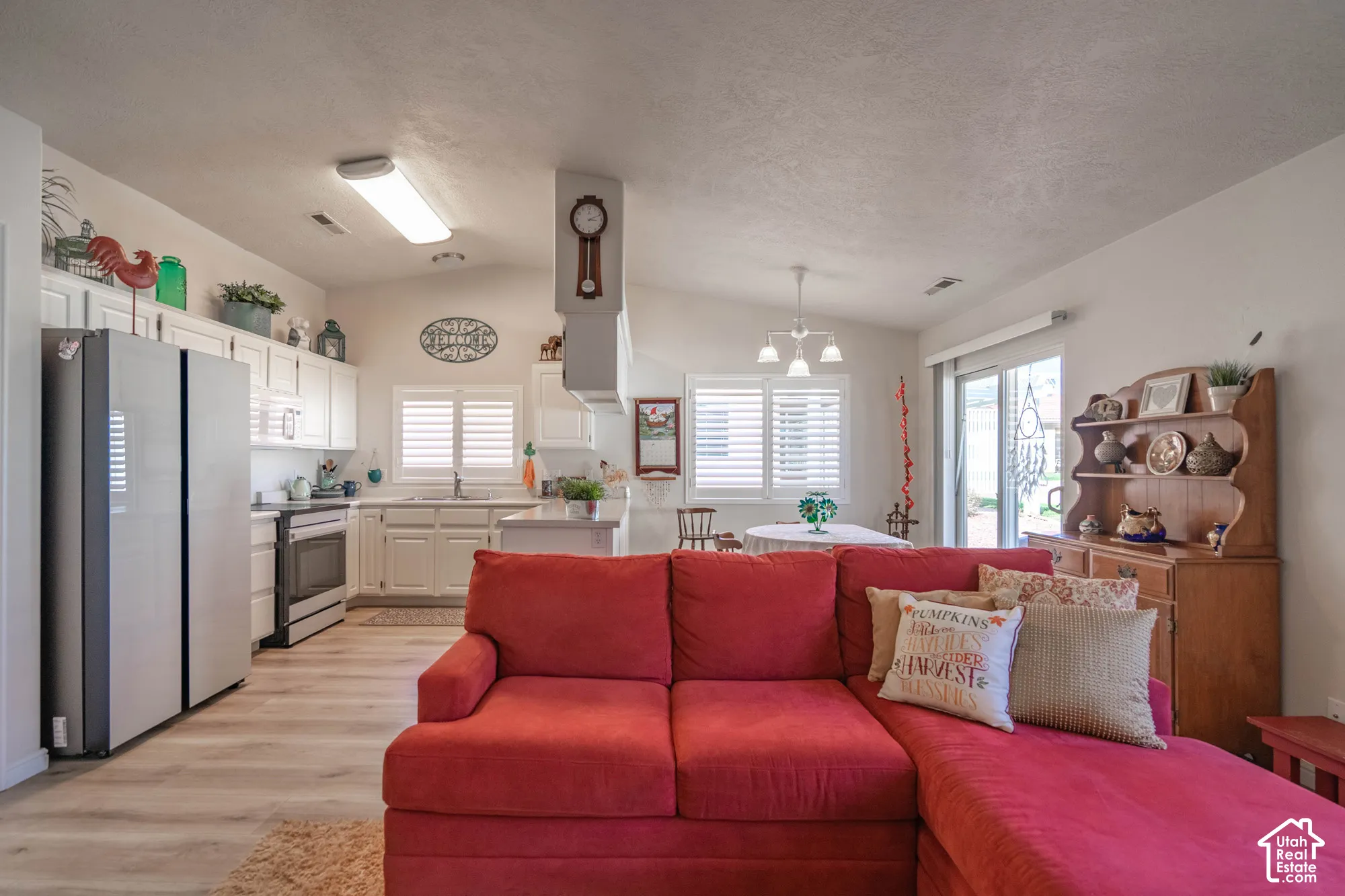 Open-concept living area with vaulted ceilings, wood-finish flooring, and white kitchen cabinetry