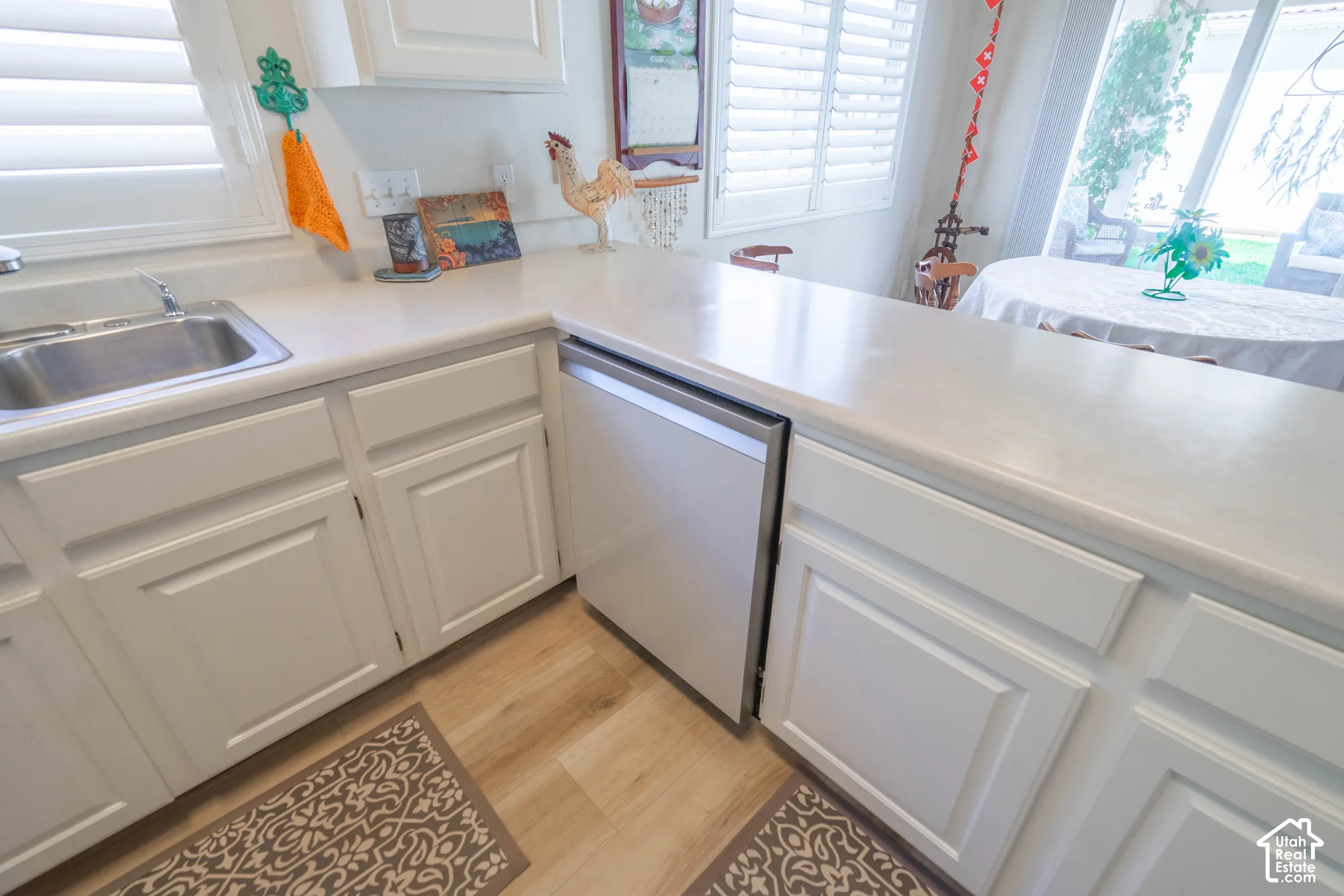 White cabinetry with panel doors, stainless steel sink, light-toned countertops, and wood-finish flooring