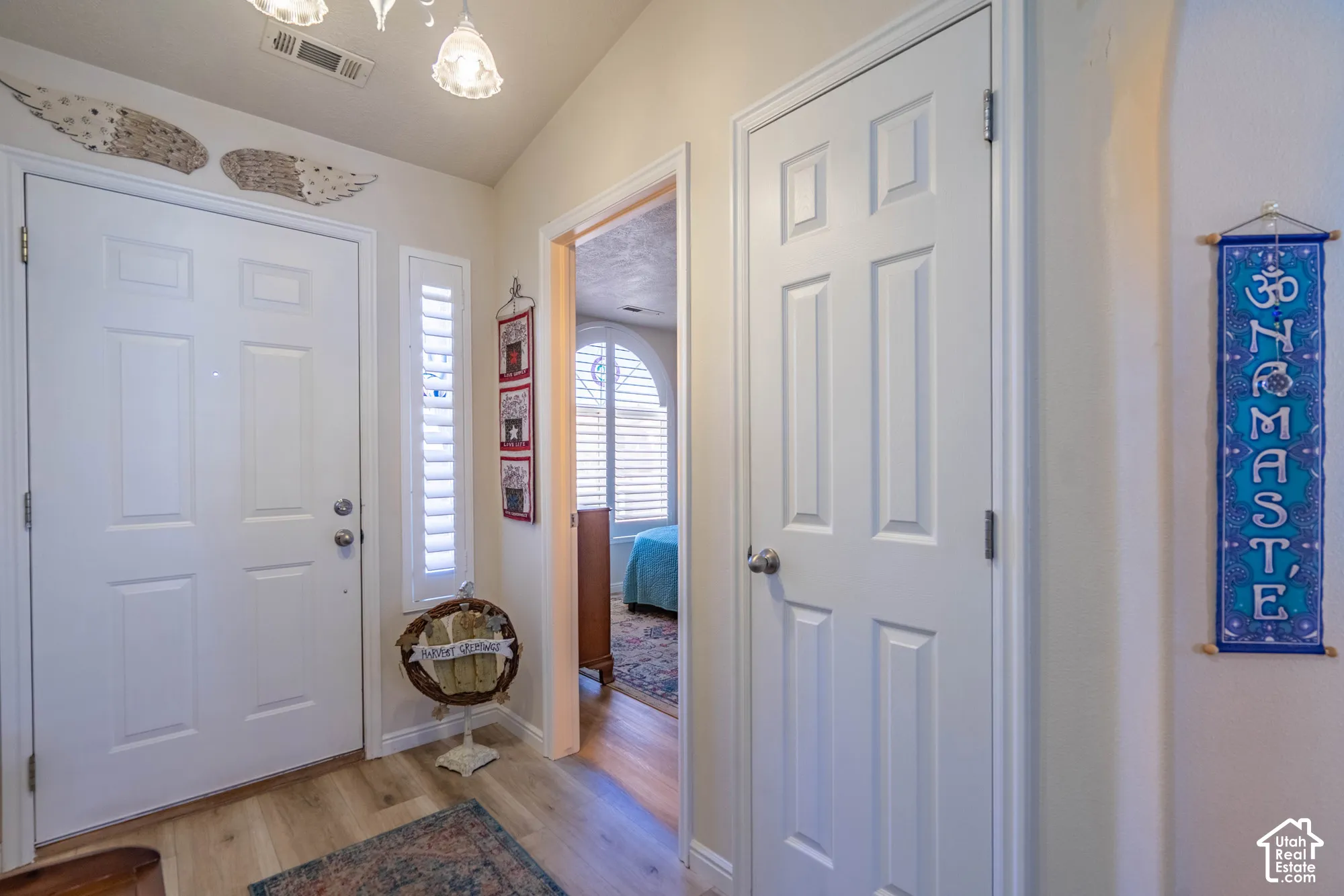 Wood-finish flooring with a white paneled entry door and a sidelight with louvered shutters