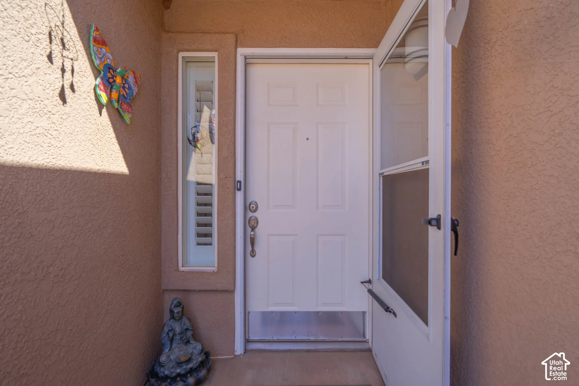 Textured exterior wall finish with a white entry door, a white screen door, and a vertical window with louvered blinds